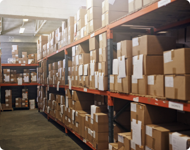 Rows of cardboard boxes neatly organized on red metal shelves in a warehouse.